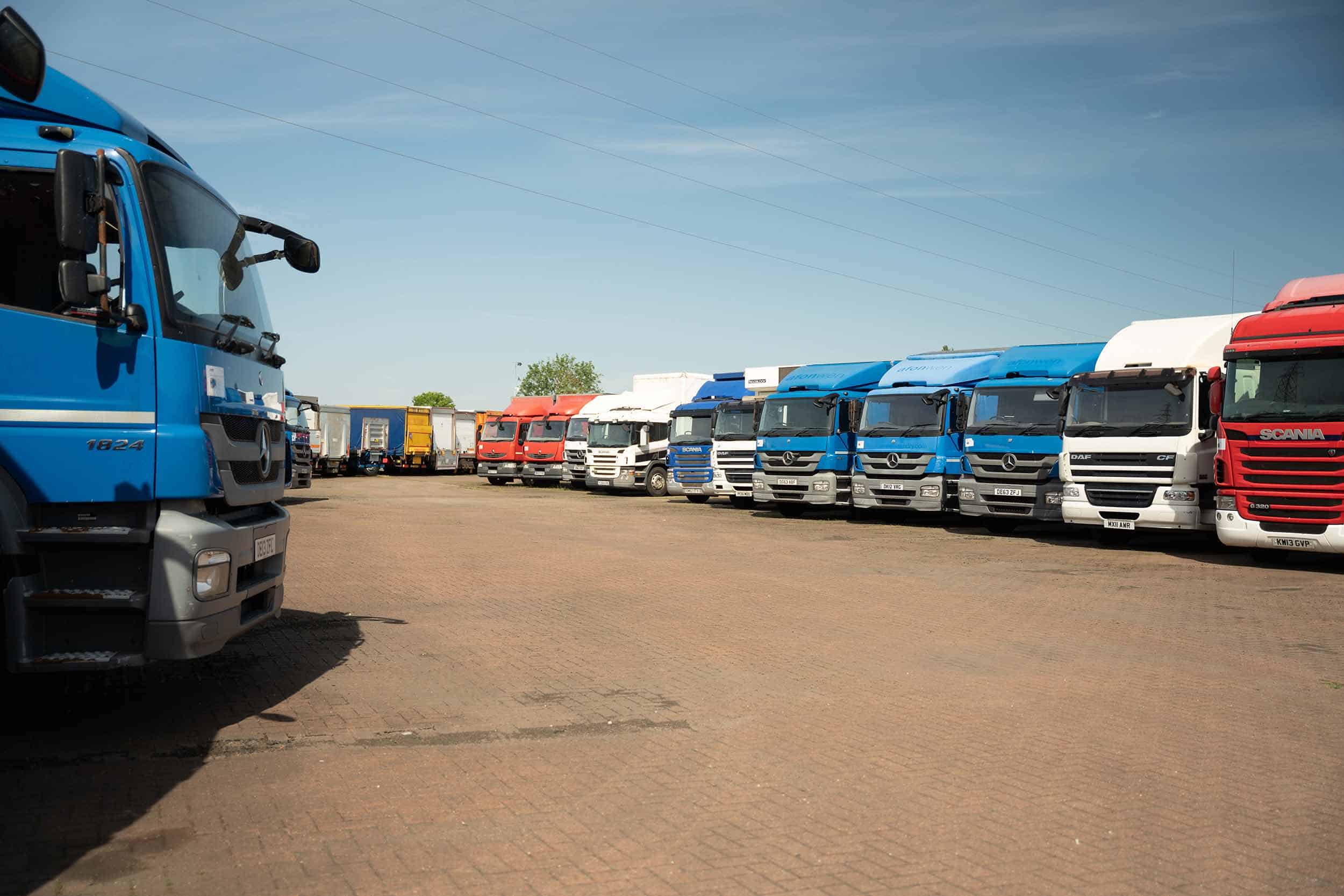 a large selection of used heavy goods vehicles in a forecourt, parked in an orderly fashion